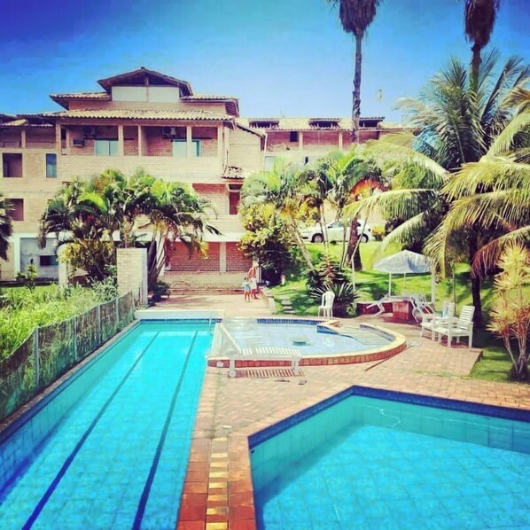 A swimming pool with two lanes, surrounded by palm trees and a building with multiple balconies.
