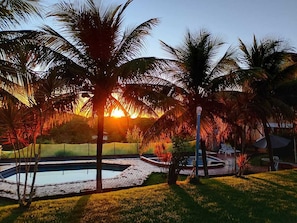 A pool area with palm trees and a sunset. - Pousada Herva Doce (Rio das Ostras)