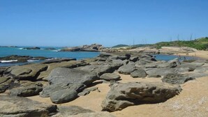 A rocky beach with large boulders and a clear blue sky. - Pousada Herva Doce (Rio das Ostras)