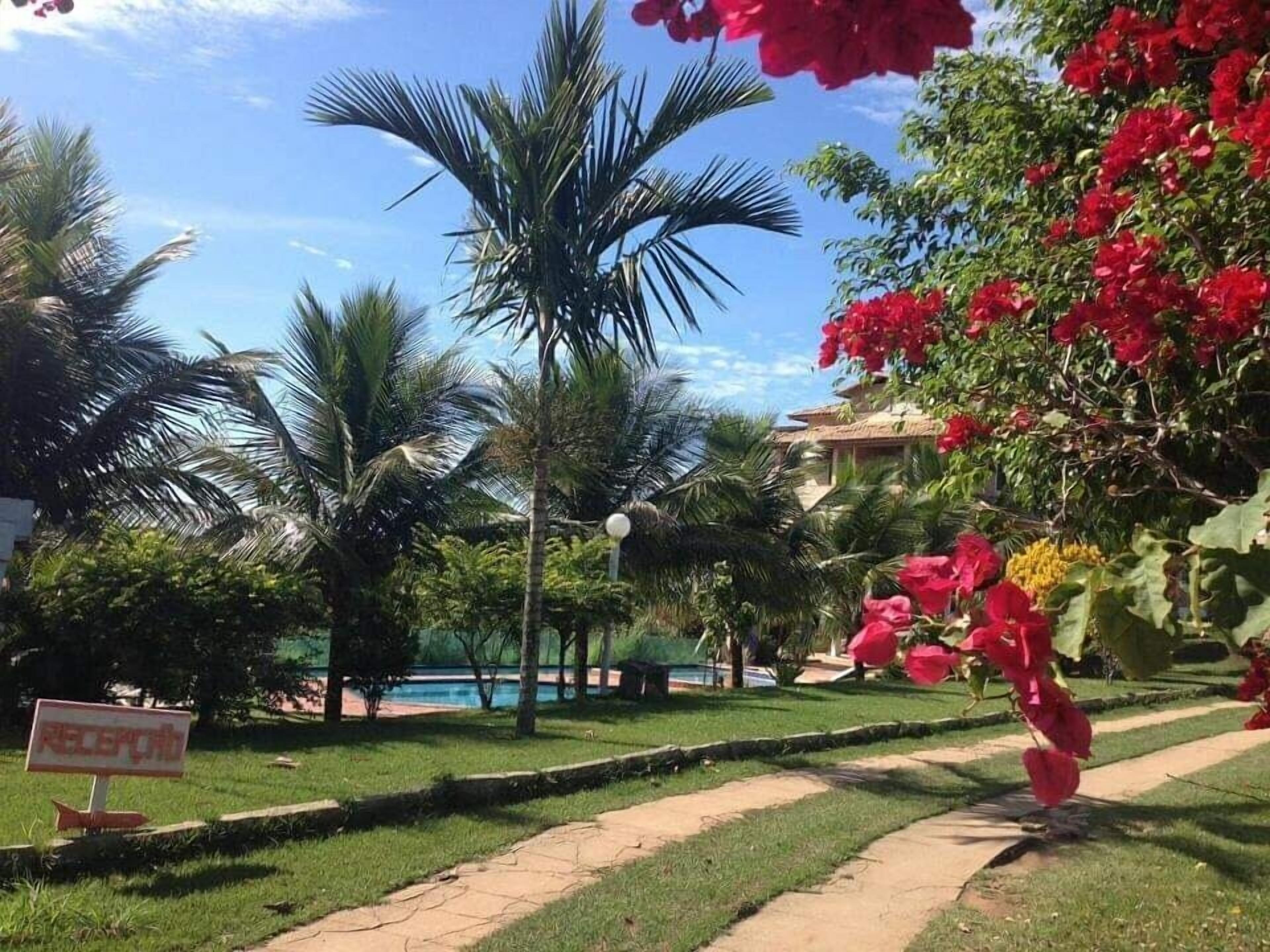 A landscaped garden with palm trees, red flowers, and a pathway leading to a building.