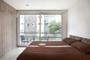 Relax in a spacious bedroom with a large bed and sliding glass door leading to a balcony with a dining table and city views.