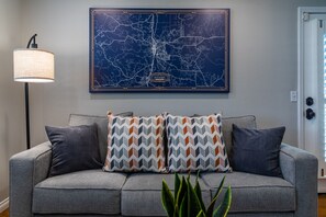 A gray sofa with patterned cushions, a map on the wall, and a floor lamp.