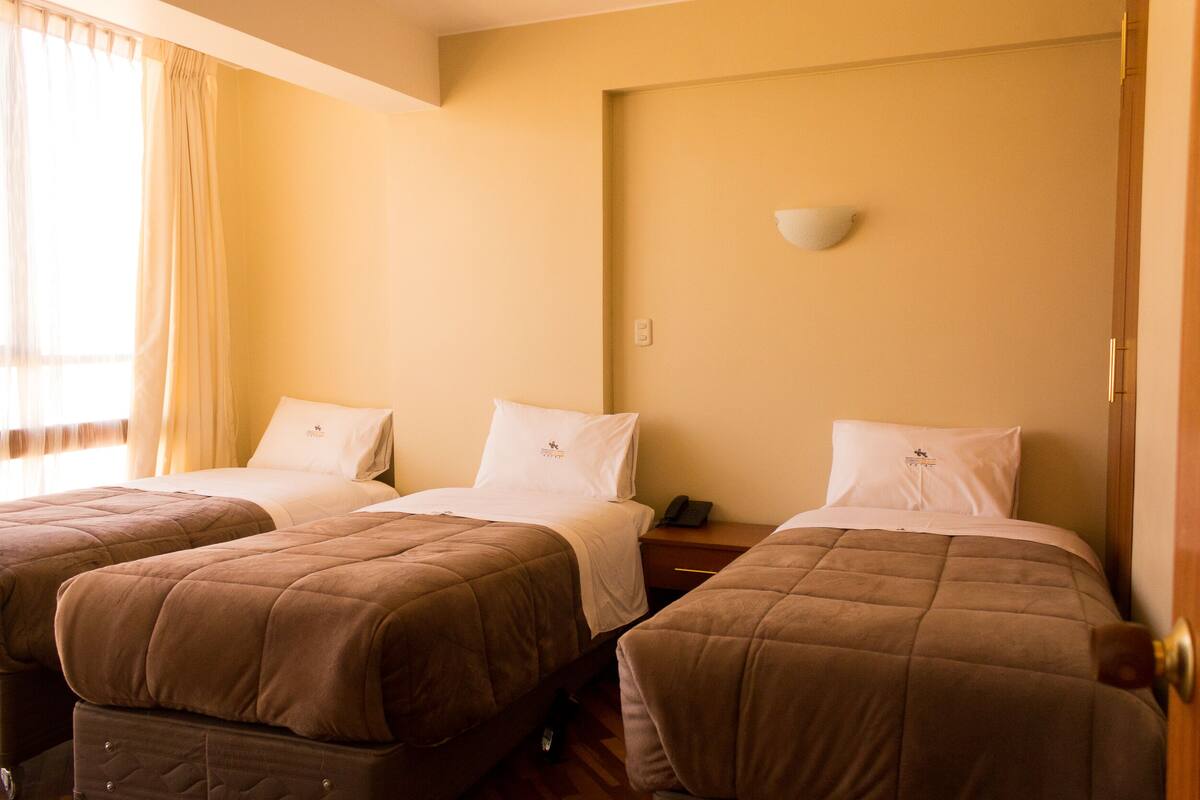 Ein Hotelzimmer mit zwei Betten, jeweils mit einer braunen gesteppten Bettdecke und weißen Kissen. Ein Nachttisch mit Lampe und Telefon ist vorhanden.