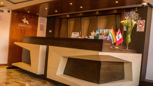 A hotel reception desk with a modern design, featuring a wooden accent wall and a glass display case. - Hotel Cusco Dreams (Cusco)