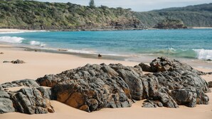 Ein felsiger Strand mit klarem, blauem Wasser und einer hügeligen Landschaft im Hintergrund.