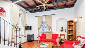 Una sala de estar con un sofá rojo, una mesa de centro de madera, un ventilador de techo y una escalera con barandilla.