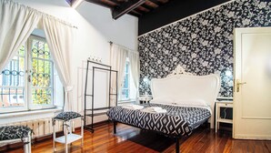 Un dormitorio con cama, ventana con cortinas, radiador y papel tapiz estampado.