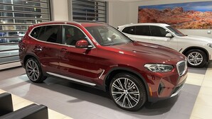 Un SUV vermell en un saló d'exposició amb altres vehicles, finestrals amplis i un quadre mural que representa un paisatge desèrtic.
