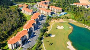 Vista aérea de un complejo turístico con varias edificaciones, un campo de golf y una masa de agua.