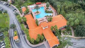 Vista aérea de un hotel con piscina, palmeras y una carretera curva.