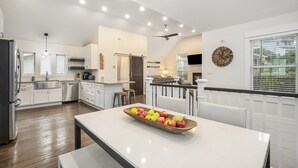 A modern kitchen with white cabinetry, a wooden dining table with a fruit bowl, and a ceiling fan. - "Let it B" Luxury lake home in South Haven MI. Just steps to N beach. Sleeps 8. (South Haven)