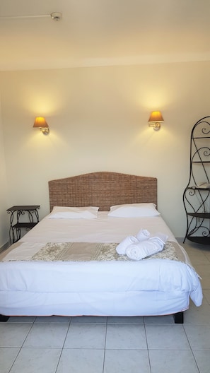 A neatly made bed with white linens, two wall-mounted lamps, a woven headboard, a small table, and a metal stand with a phone. - Hotel Restaurant le Bellevue (Propriano)