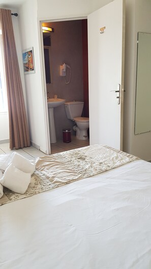 A hotel room with a bed, a bathroom visible through an open door, a telephone, and a trash bin. - Hotel Restaurant le Bellevue (Propriano)