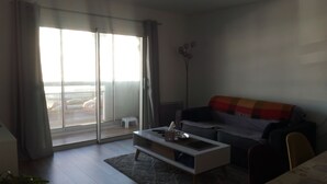 A living room with a sofa, a coffee table, and a view of the sea through large windows.