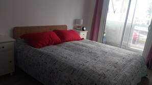 A bedroom with a bed, two red pillows, a nightstand with a lamp, and a window with curtains.