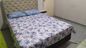A bedroom with a floral bedspread, a tufted headboard, a bedside table, and a door. - Pousada São Miguel (Juazeiro do Norte)