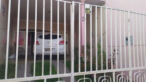 A white car parked in a gated driveway with a pink wall and a sign indicating a motor repair shop. - Pousada São Miguel (Juazeiro do Norte)