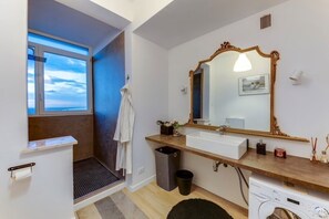 A modern bathroom with a large mirror, a sink, a shower, and a window with a view.