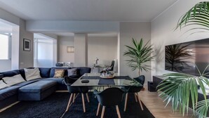 A modern living room with a sectional sofa, a glass dining table, and black chairs. There is a large potted plant and a flat-screen TV mounted on the wall. - SUPER SEA VIEW PENTHOUSE (Rimini)