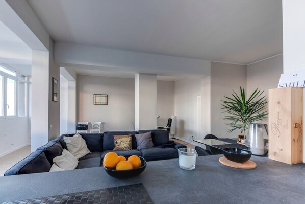 A modern living room with a dark grey sofa, a coffee table with a bowl of oranges, and a minimalist design.