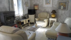 Een woonkamer met een bank, fauteuils, een televisie, een open haard en een lamp.