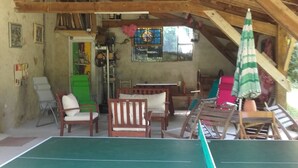 Een rustiek houten interieur met een tafeltennistafel, houten stoelen en een groene tafel.
