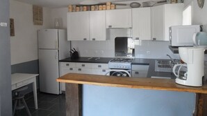 Een kleine keuken met witte kastjes, een gasfornuis, een magnetron en een koffiezetapparaat.