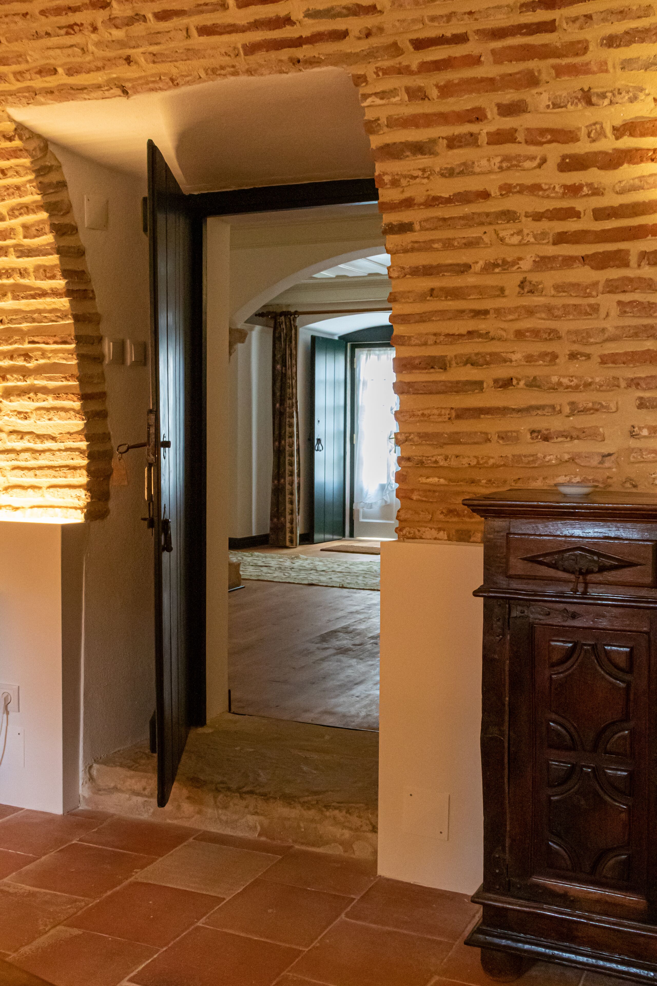Un couloir avec un mur en briques, une armoire en bois et une porte donnant sur une autre pièce.