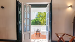 An open doorway leading to a patio with a table and chairs, a wooden chair, and a wall-mounted light fixture. - Quinta da Foz (Caldas da Rainha)
