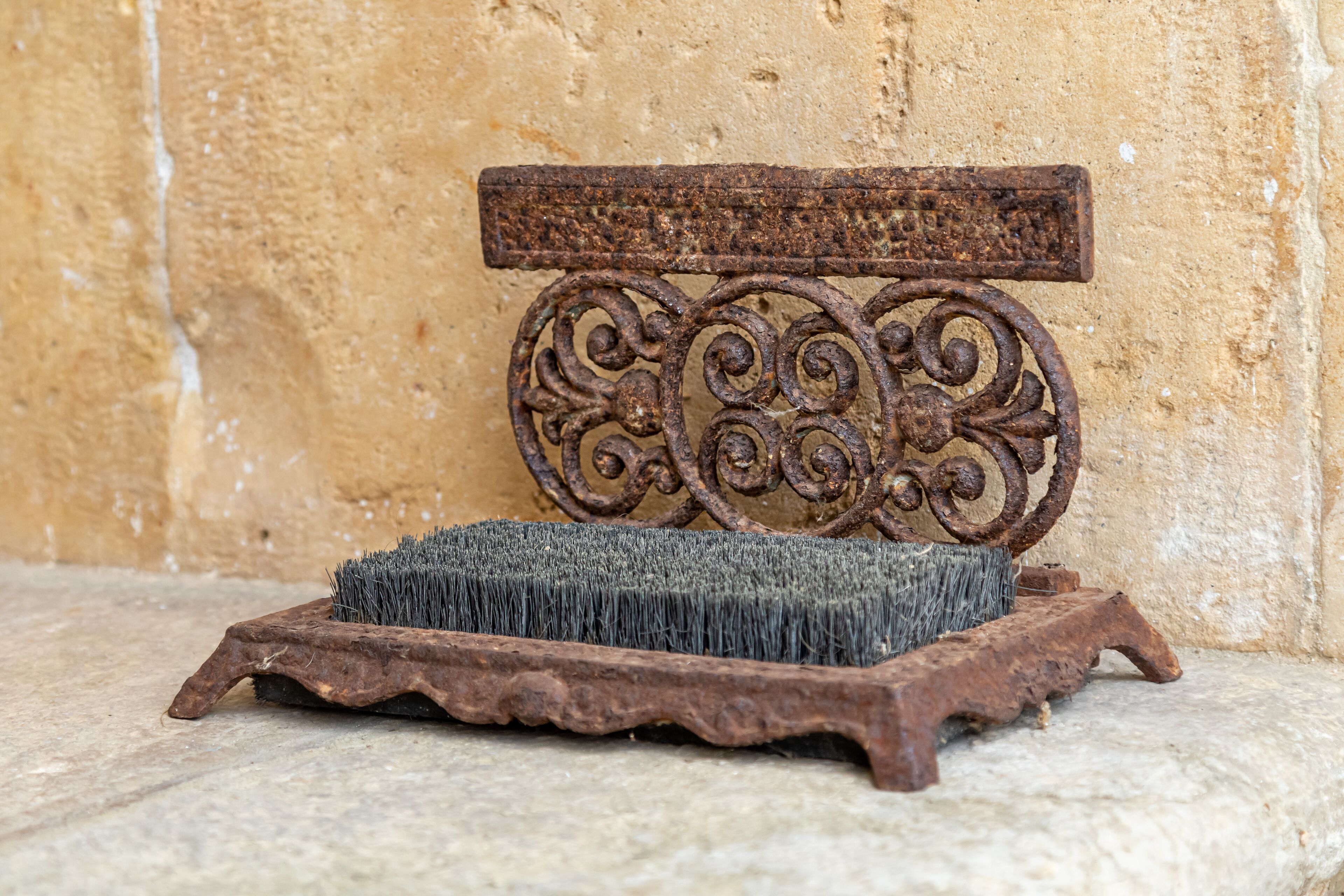 A rustic metal bench with intricate scrollwork against a textured wall.