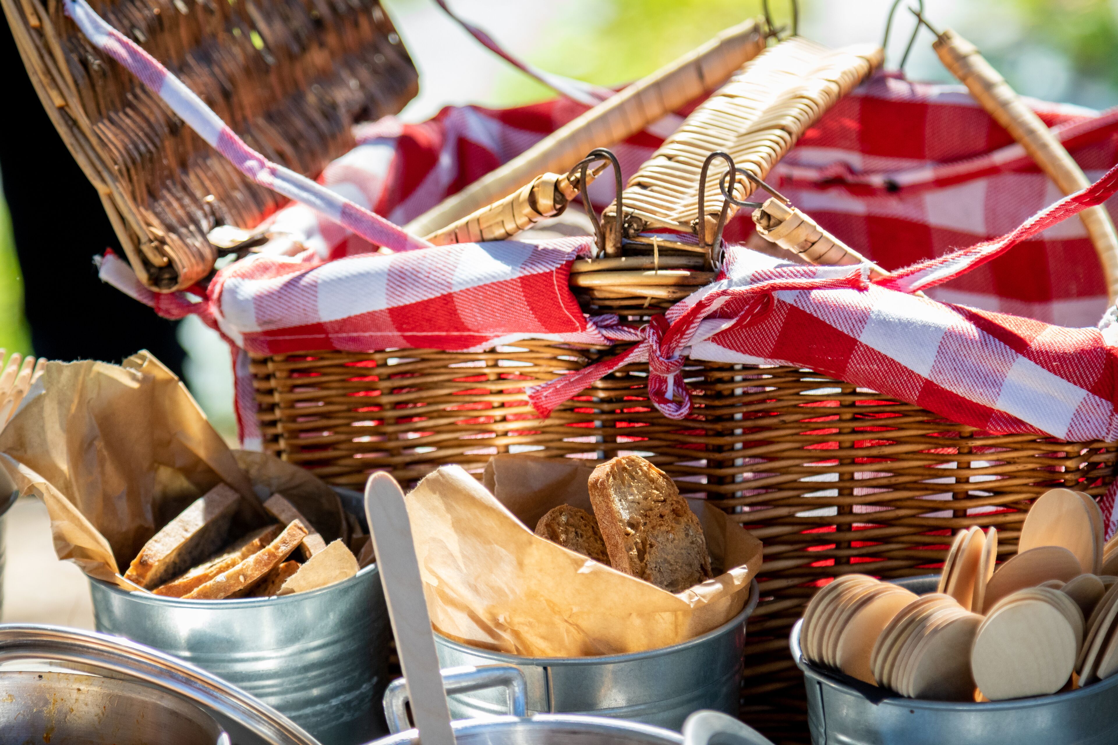 A picnic setup with a wicker basket, metal containers, and a checkered cloth.