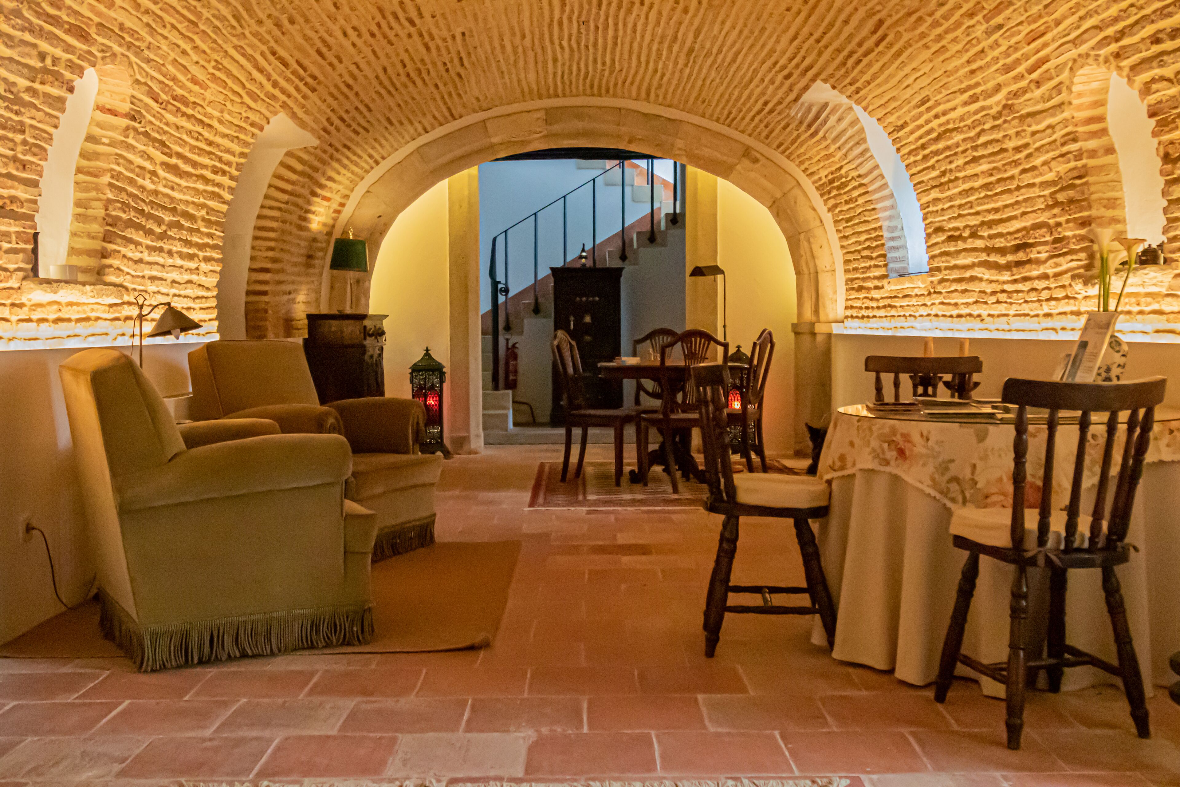 Un ambiente acogedor con un arco de piedra que conduce a una escalera, un comedor con mesa y sillas, y una sala de estar con sofás y alfombra.