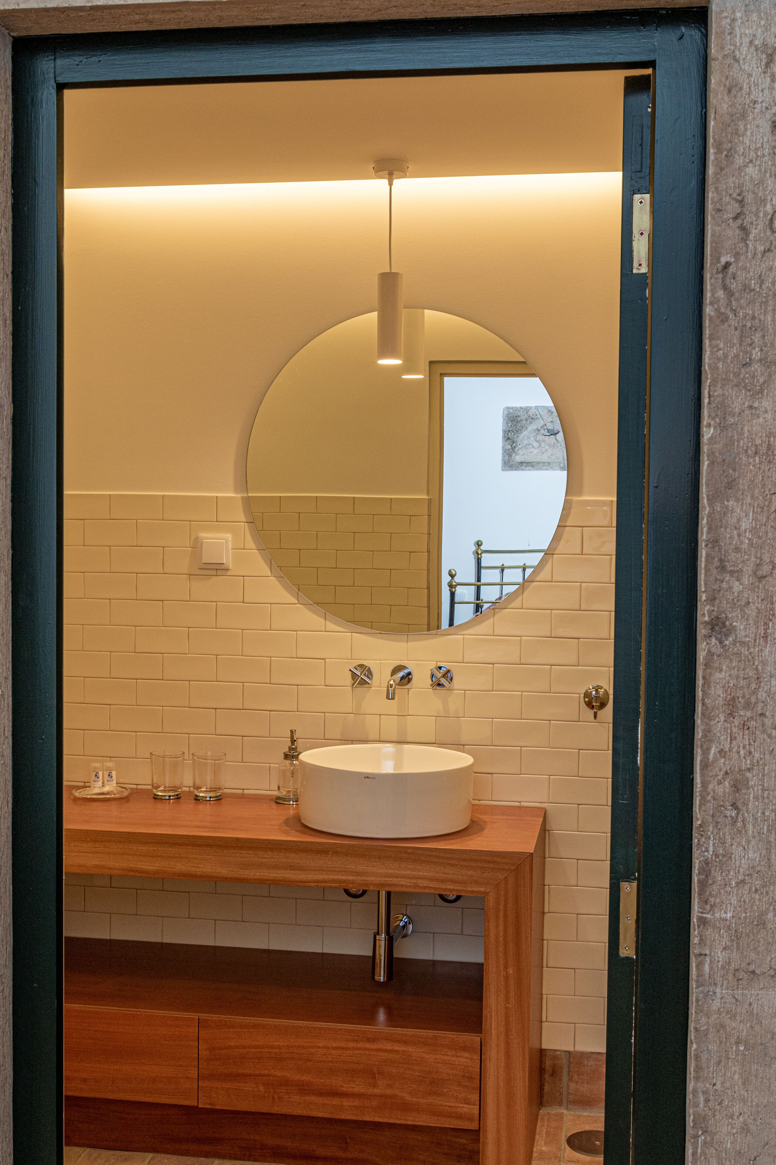 A bathroom with a round mirror, white sink, and wooden vanity.