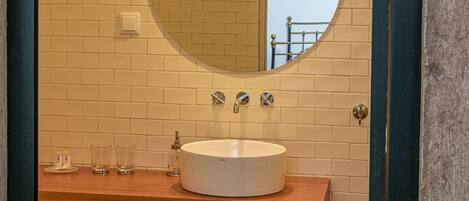 A bathroom with a round mirror, white sink, and wooden vanity.