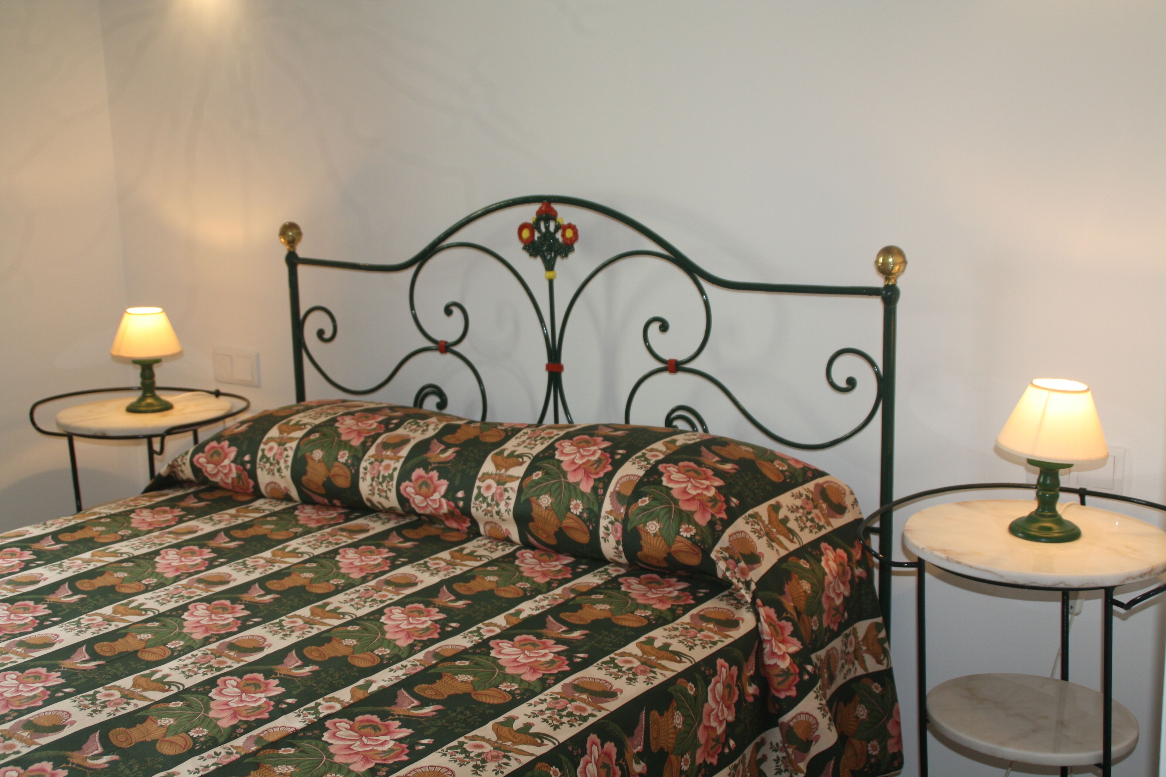 Una cama con colcha estampada, dos mesitas de noche con lámparas y un cabecero decorativo de metal.