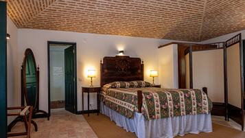 A bedroom with a brick ceiling, a bed with floral bedding, two bedside lamps, a wooden headboard, and a large mirror.