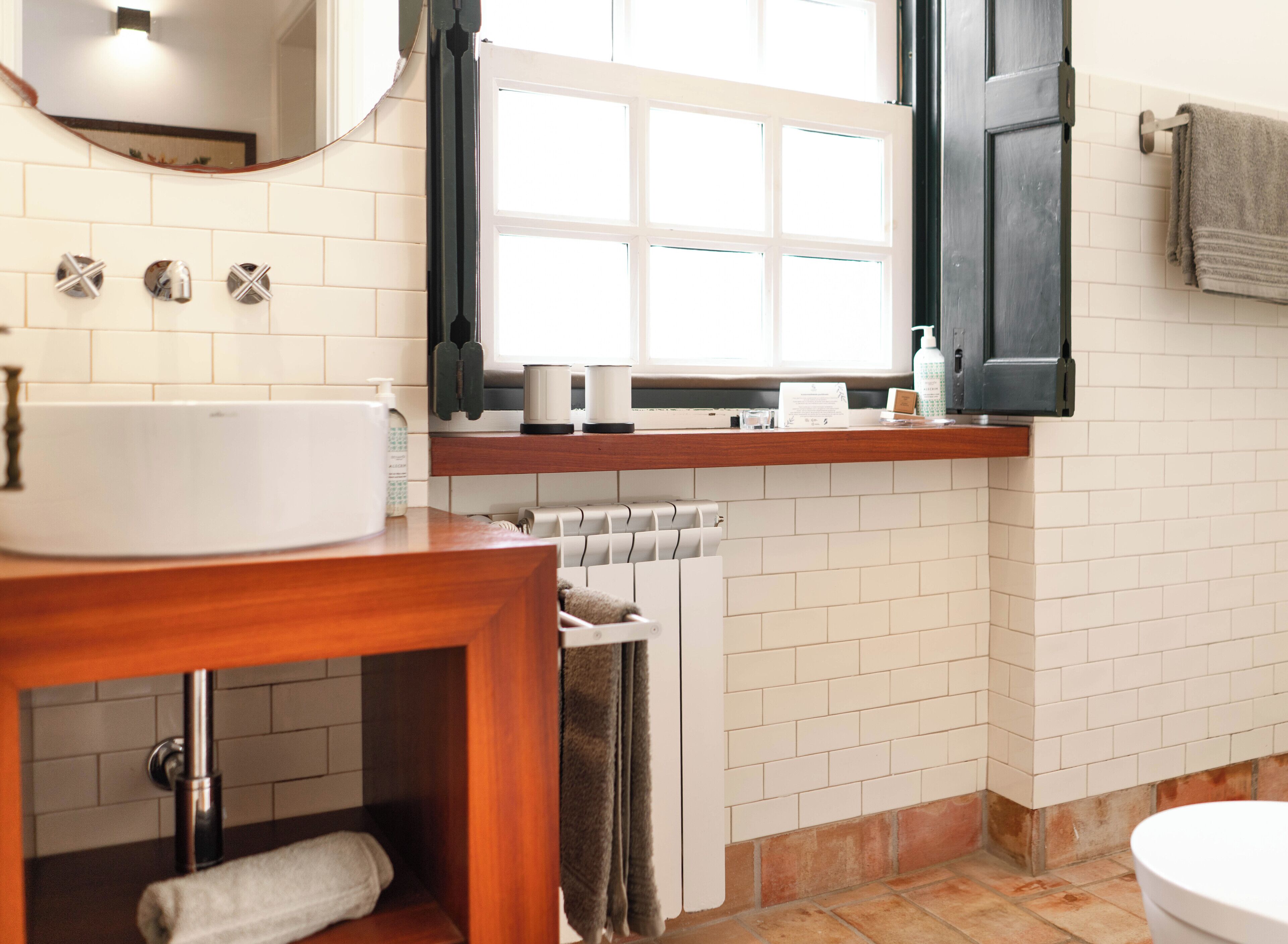 A bathroom with a white sink, a mirror, a window with black shutters, a towel rack, and a toilet.