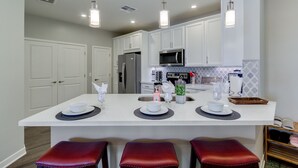 A modern kitchen with white cabinets, a central island with bar stools, stainless steel appliances, and pendant lighting. - Relax in 2 bedroom Condo at The Cays Ocotillo!30 Night Min! (Chandler)