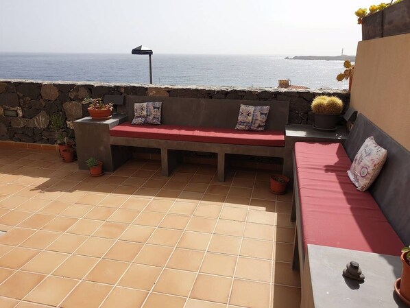 A terrace with a red bench, potted plants, and a view of the sea.