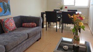 A living room with a grey sofa, a coffee table with a vase of flowers, a dining area with a table and chairs, and a painting on the wall. - Nice new Duplex with big terraces, whith very nice seaviews. For your relax (Porís de Abona)
