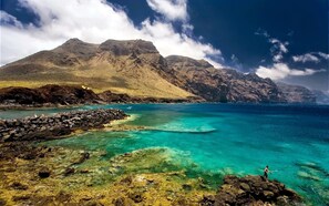 A coastal landscape with clear turquoise waters, rocky shorelines, and a mountain in the background.