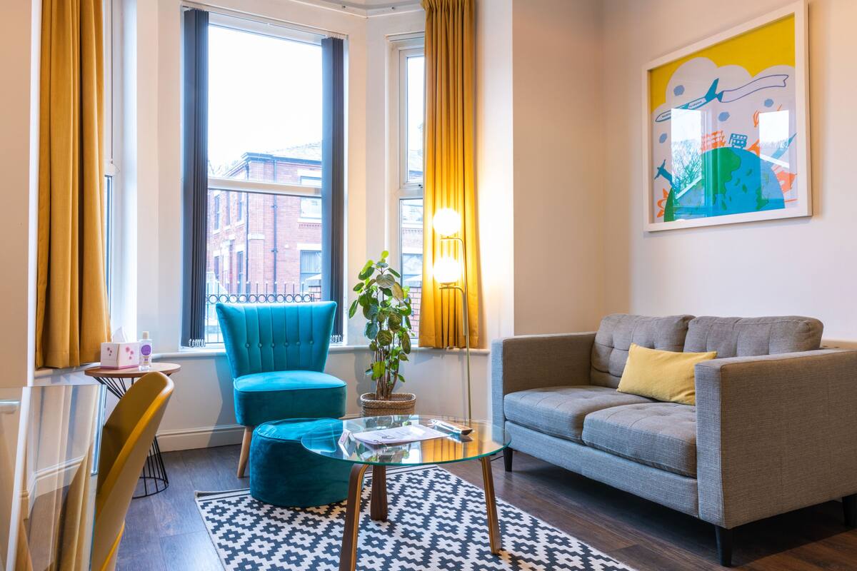 A modern living room with a grey sofa, a blue armchair, a glass coffee table, and a potted plant.
