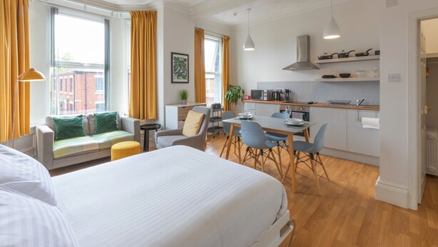 A modern hotel room with a large bed, a sofa, a dining area, and a kitchen. - Fulwood Heights (Preston)