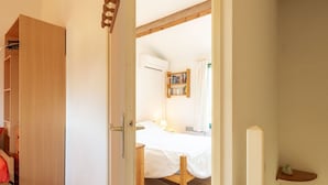 A bedroom with a wooden bed frame, a bedside table, a small shelf with books, and a wardrobe.