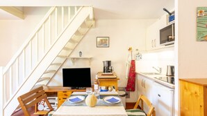 A compact kitchen with a dining area, a TV, and a staircase.