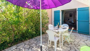 A patio with a purple umbrella, white chairs, and a table set for dining.