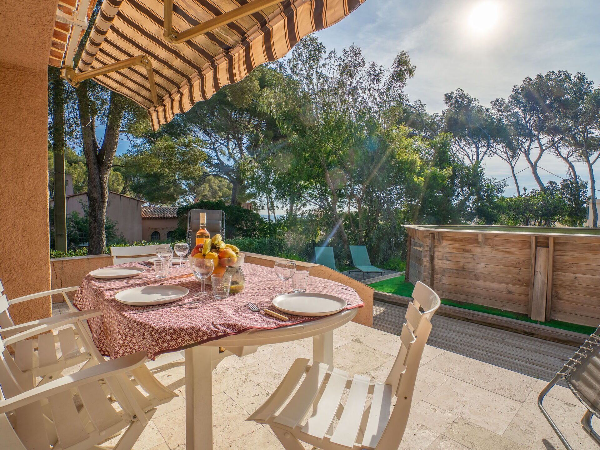 Un área de comedor al aire libre con una mesa dispuesta para cuatro personas, rodeada de sillas blancas, bajo una pérgola.