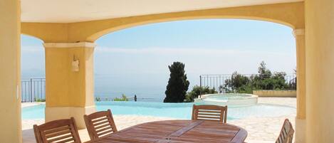 A covered outdoor area with a pool, wooden table, and chairs.