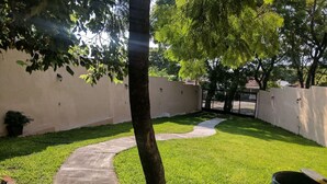 A well-maintained outdoor area with a curved concrete pathway, a tree, and a metal barrel. - Casa Jacarandas Chalet with Garden in Chapala (Chapala Haciendas)
