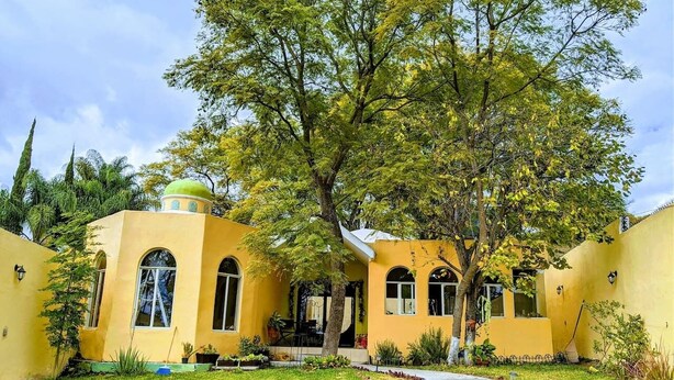 A yellow building with a dome and arched windows, surrounded by a well-maintained lawn and a curved pathway. - Casa Jacarandas Chalet with Garden in Chapala (Chapala Haciendas)